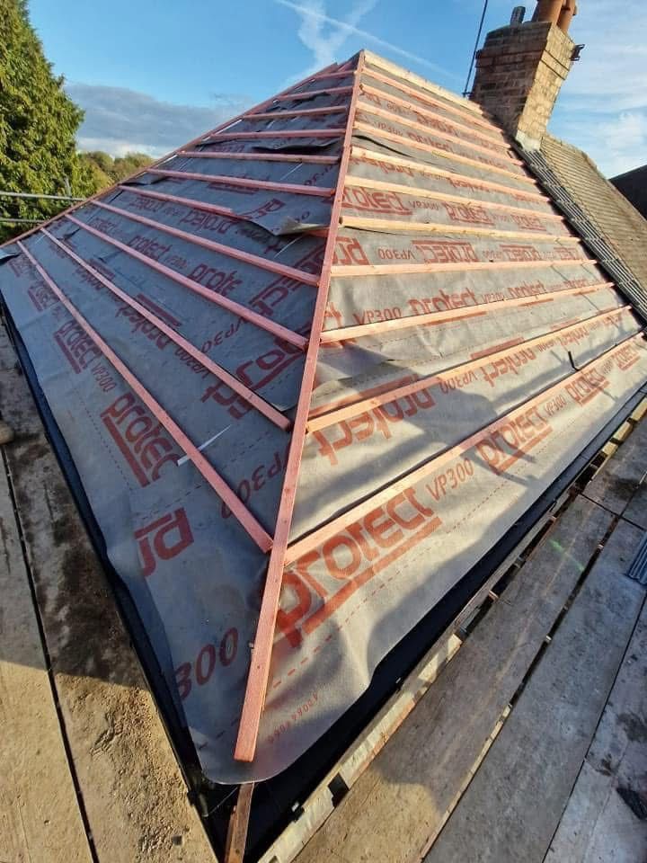 Roof under construction with reflective underlayment and a brick chimney under a blue sky