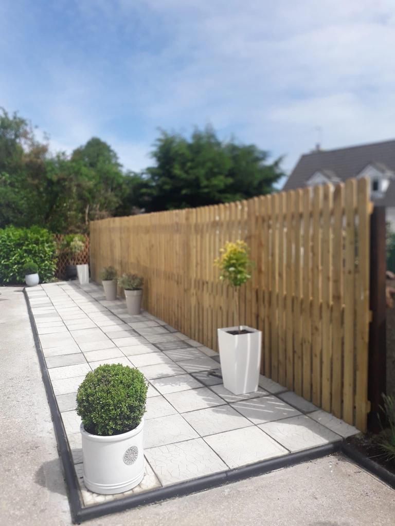 Garden patio with white pavers, potted plants, and a wooden fence under a blue sky