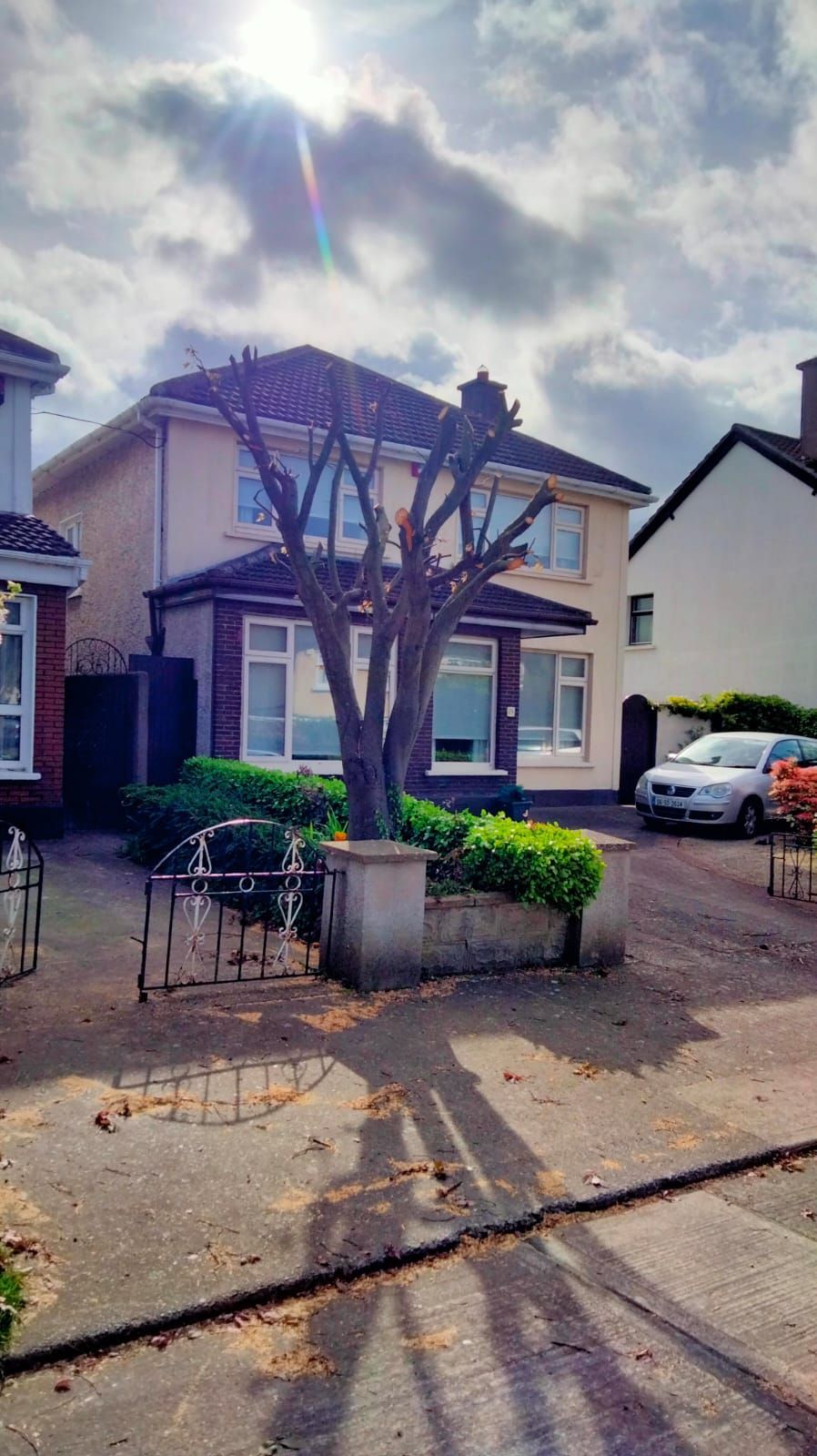 Two-story house with a leafless tree in front, a parked car, and a small patio under cloudy skies.