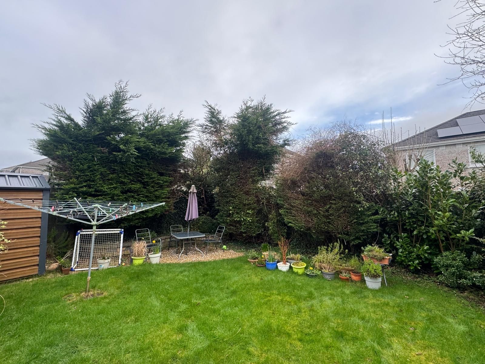 Backyard lawn with trees, patio umbrella, and garden bed under a cloudy sky