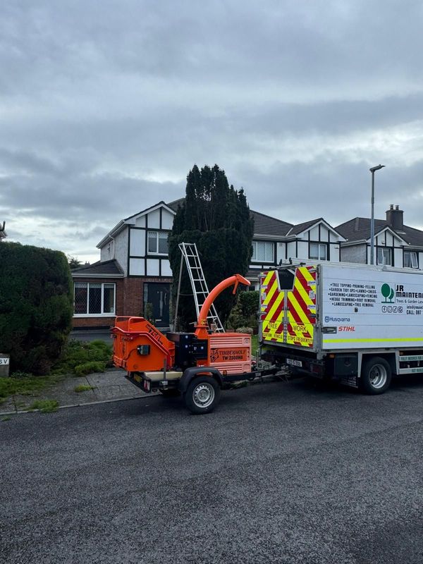 Orange chipper and work truck parked outside a house on a cloudy day.