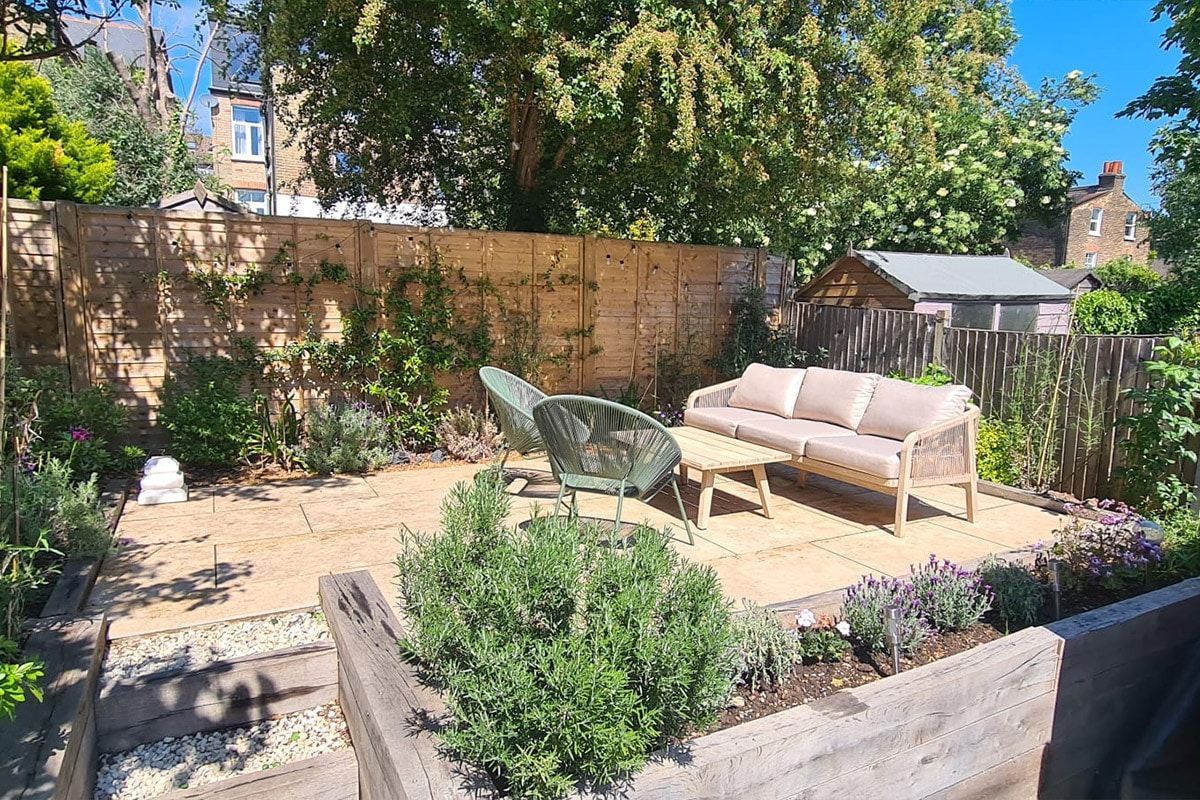 Backyard patio with beige sofa, green chair, and potted plants in bright sunlight