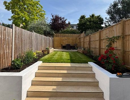 Backyard garden with stepped patio, lawn, flower beds, and tall wooden fence