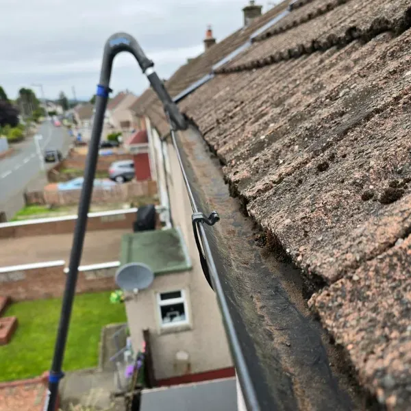 Roof edge with a vacuum hose cleaning gutters above a suburban street and houses