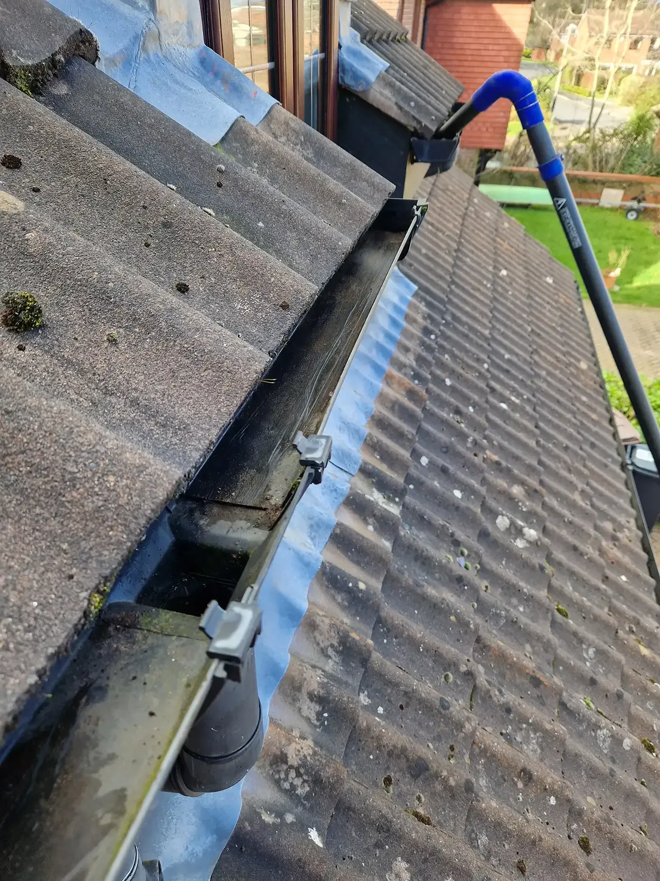 Roof gutter being cleaned beside corrugated roof panels with a long-handled brush.