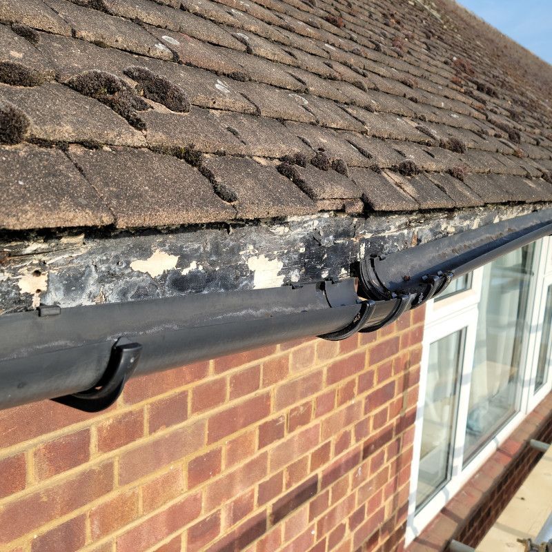 Damaged roof edge with peeling paint and gutter beside a brick house and window