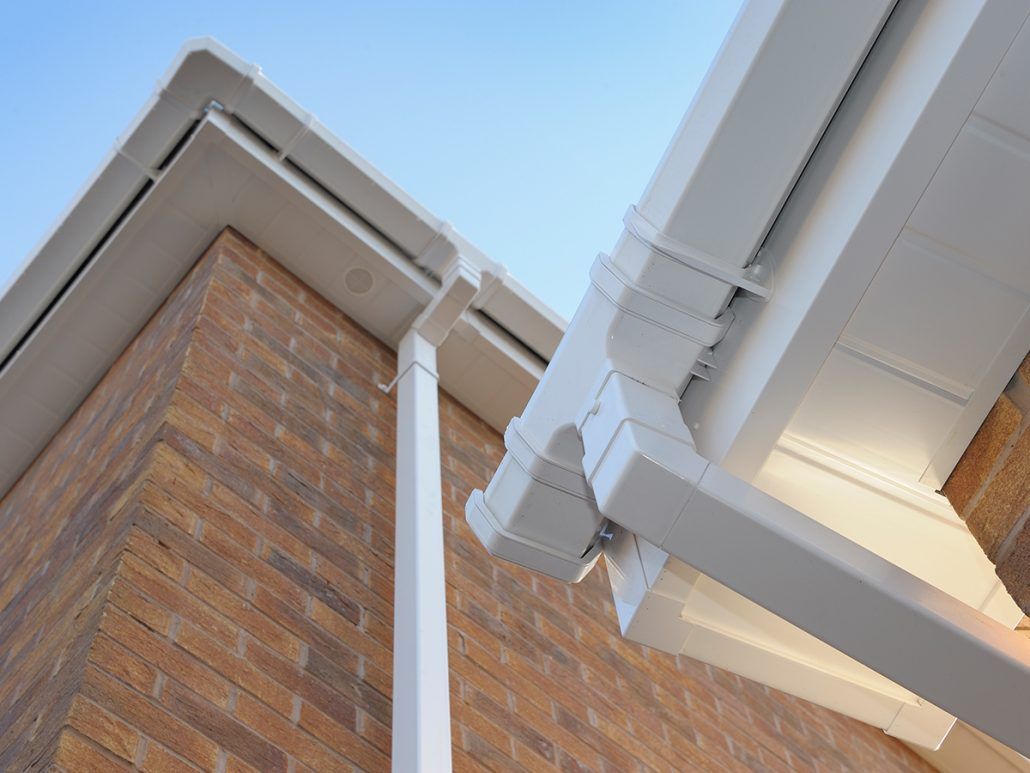 Brick house corner with white gutter and eaves against a blue sky