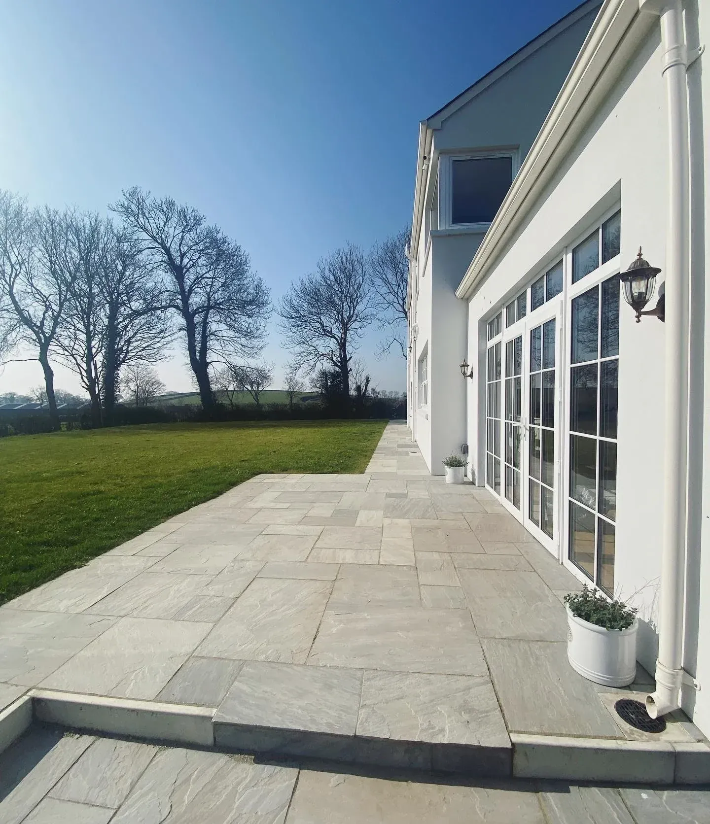 White house patio with glass doors, stone paving, and a lawn under a clear blue sky