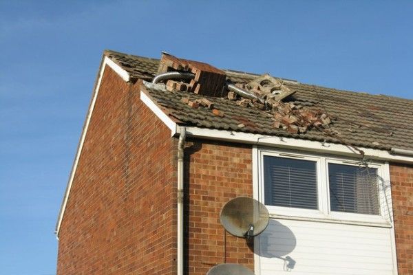 Damaged brick house roof with missing tiles and a satellite dish under a blue sky