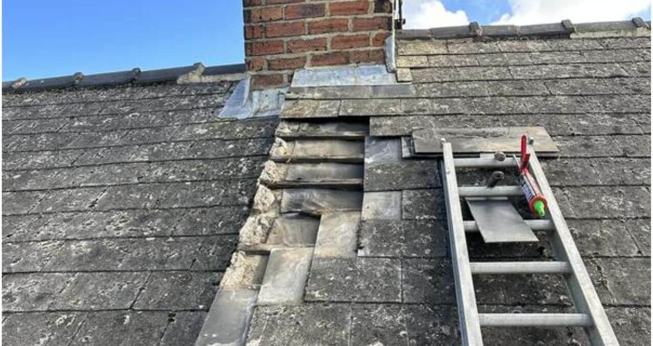 Roof with damaged gray shingles around a brick chimney and a ladder leaning on the right side.
