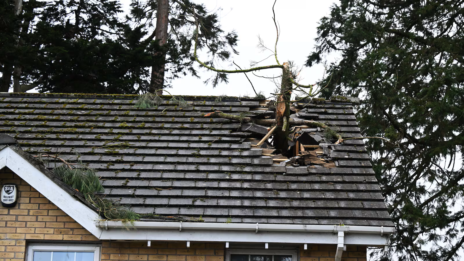 Damaged house roof with a large broken section and debris near the chimney