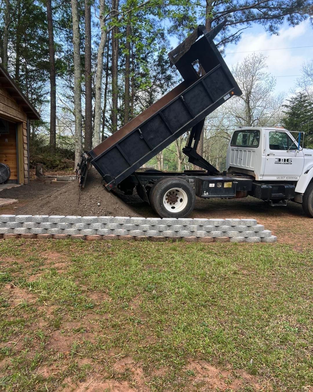 A dump truck is parked in a grassy yard with its bed up.