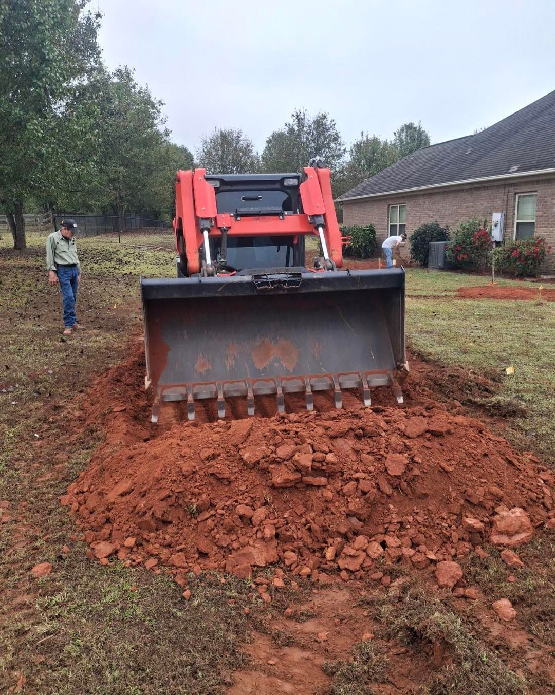 A bulldozer is moving dirt in a yard in front of a house.