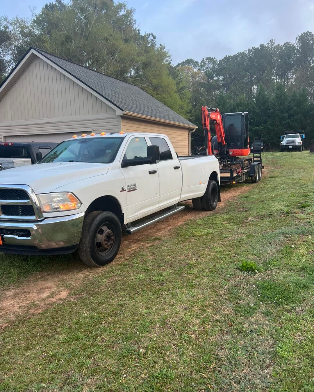 A white truck is towing a small excavator on a trailer.