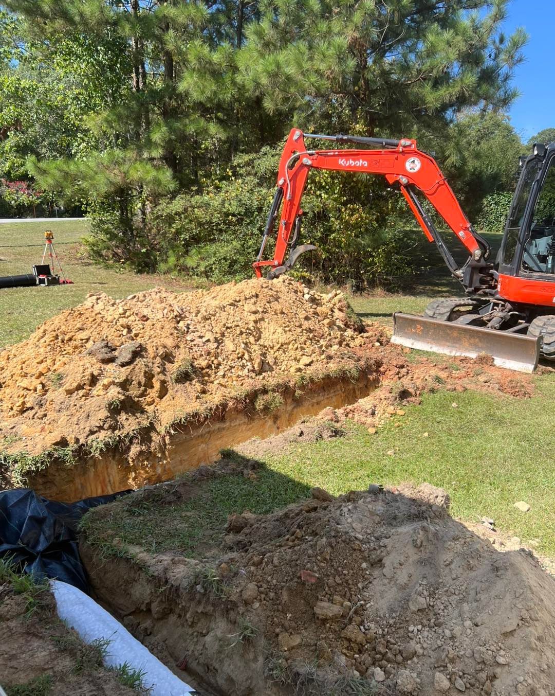 A red excavator is digging a hole in the ground in a yard.