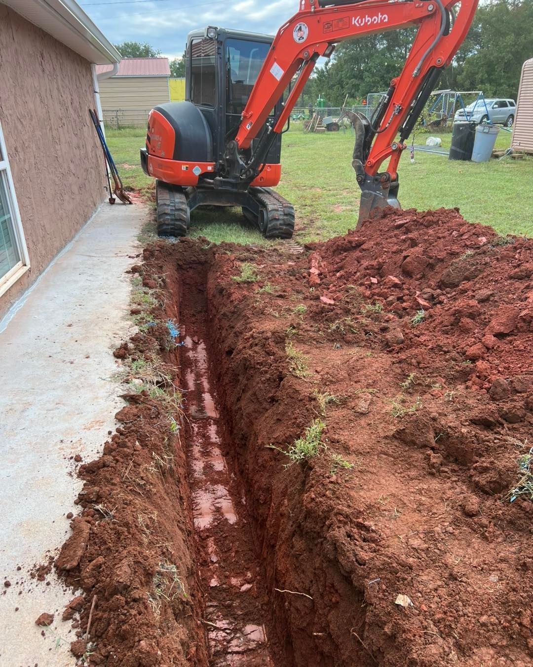 An excavator is digging a hole in the dirt in front of a house.