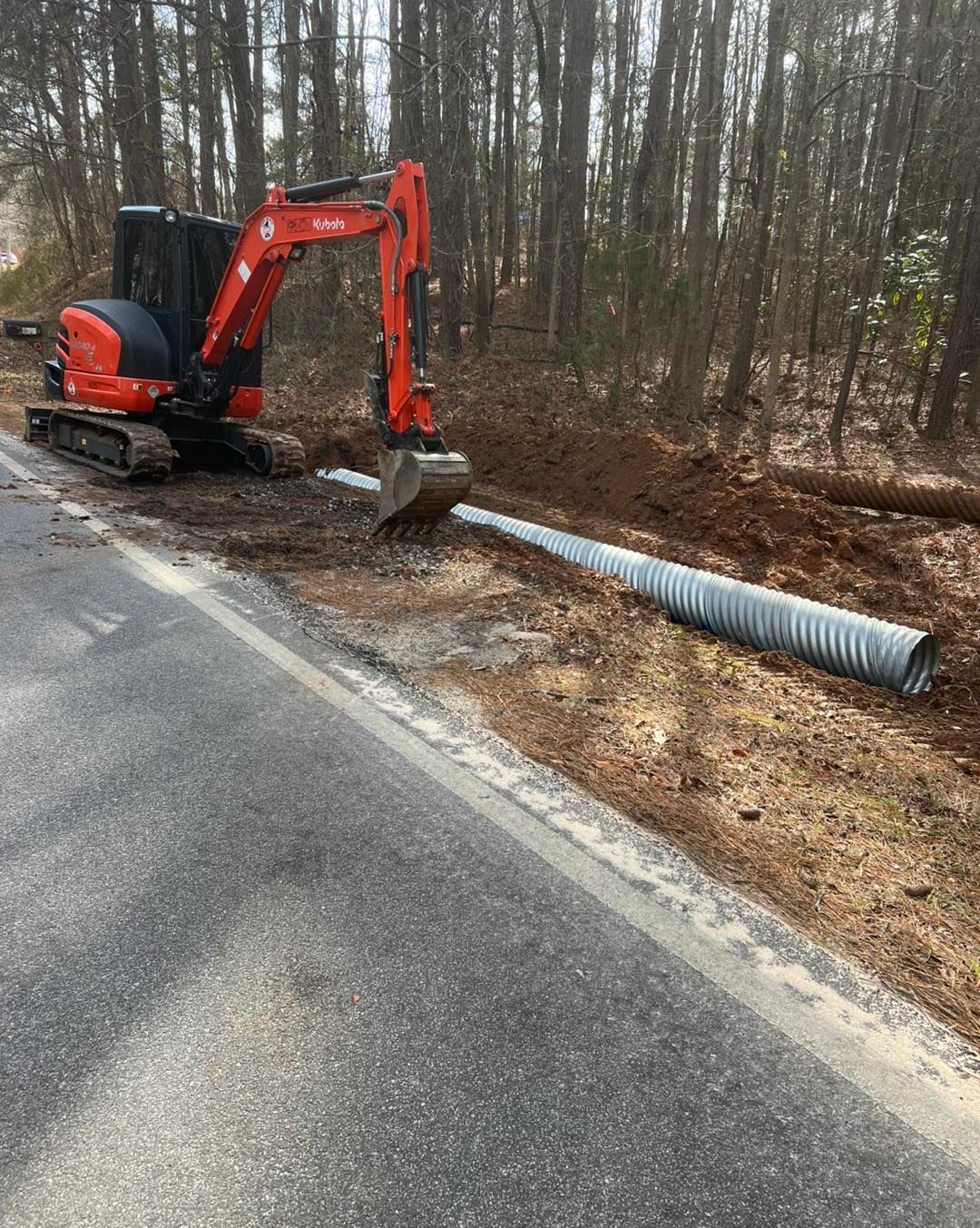 An excavator is sitting on the side of a road next to a pipe.