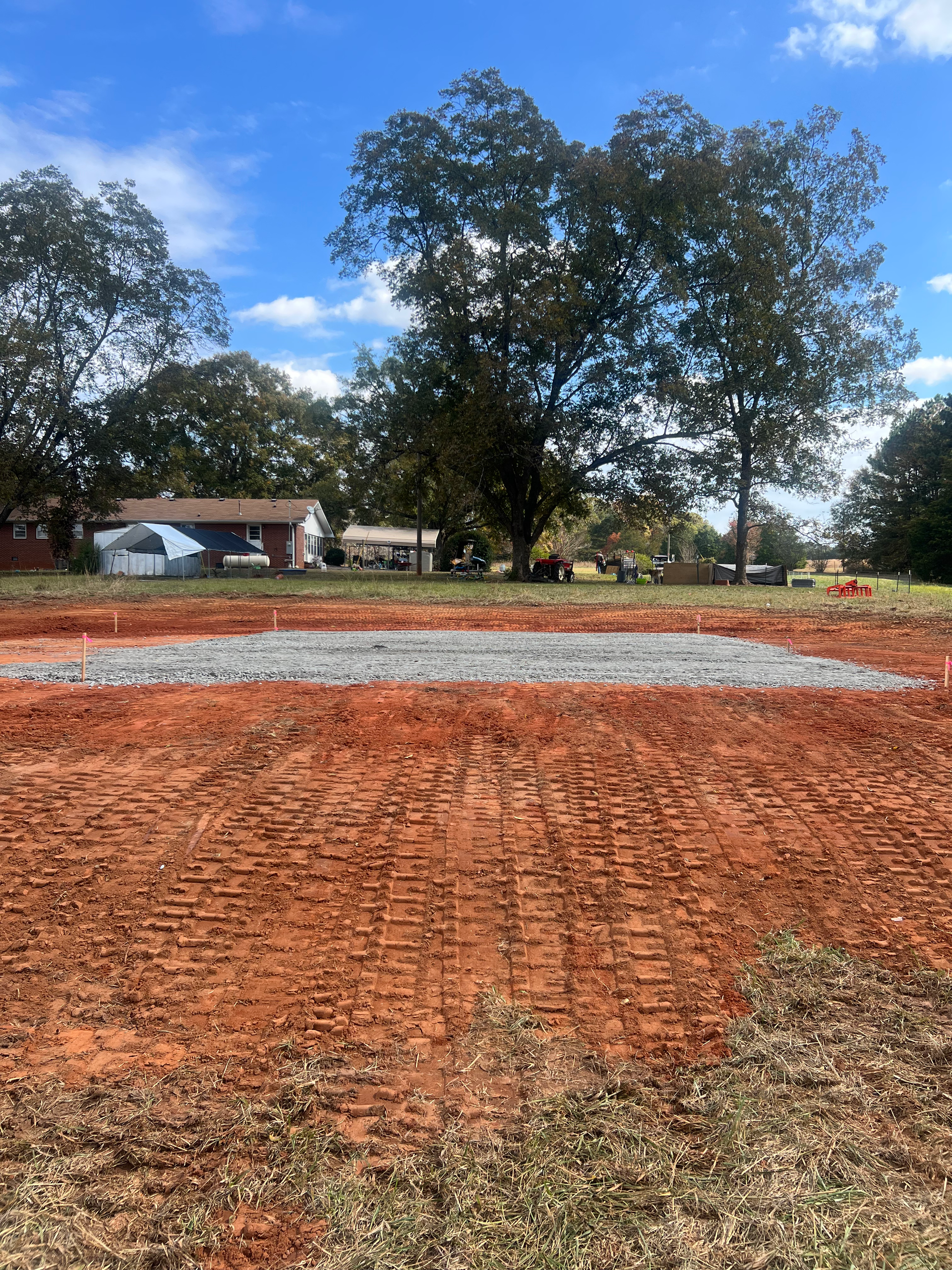 A dirt field with a house in the background and trees in the foreground.