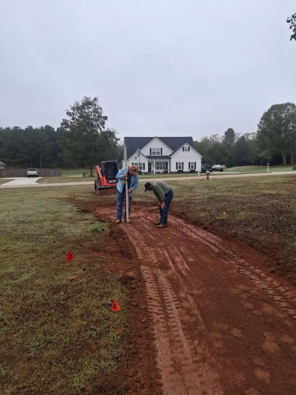 Two men are working on a dirt road in front of a house.