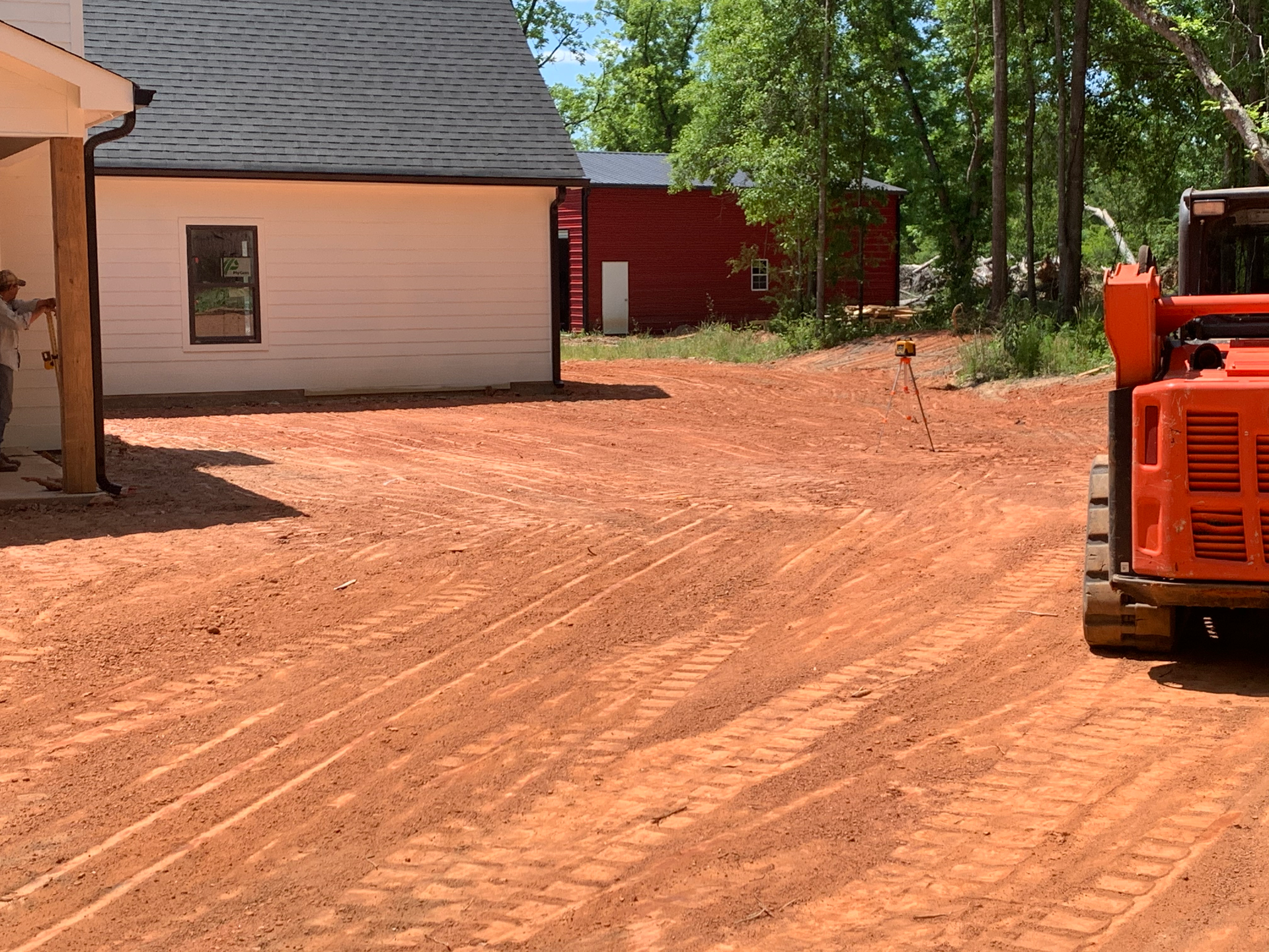 A bulldozer is driving down a dirt road in front of a house.