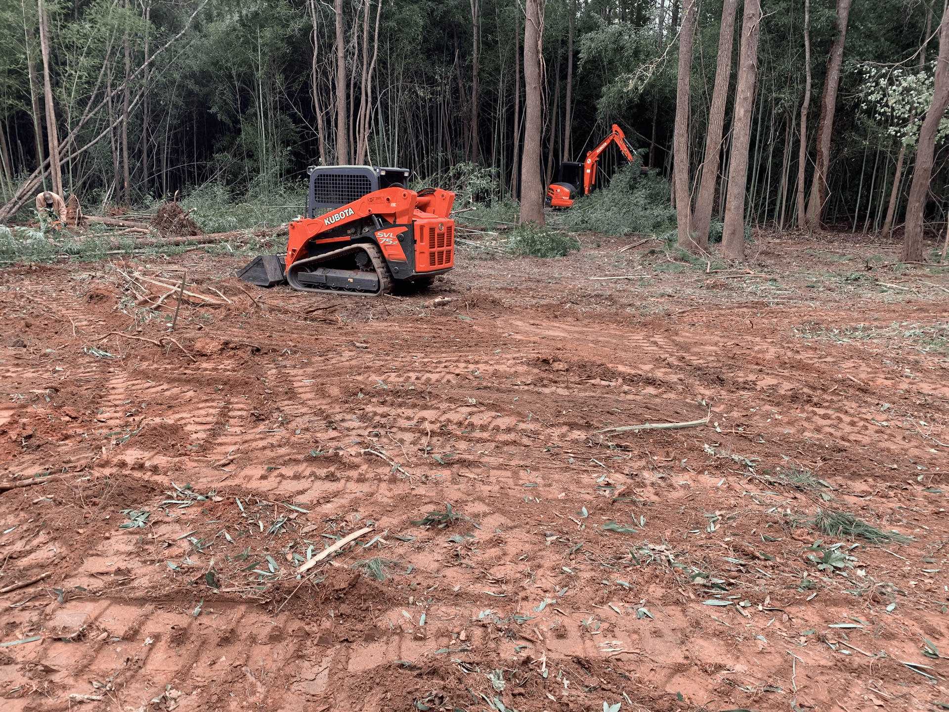 A bulldozer is driving through a dirt field in the woods.