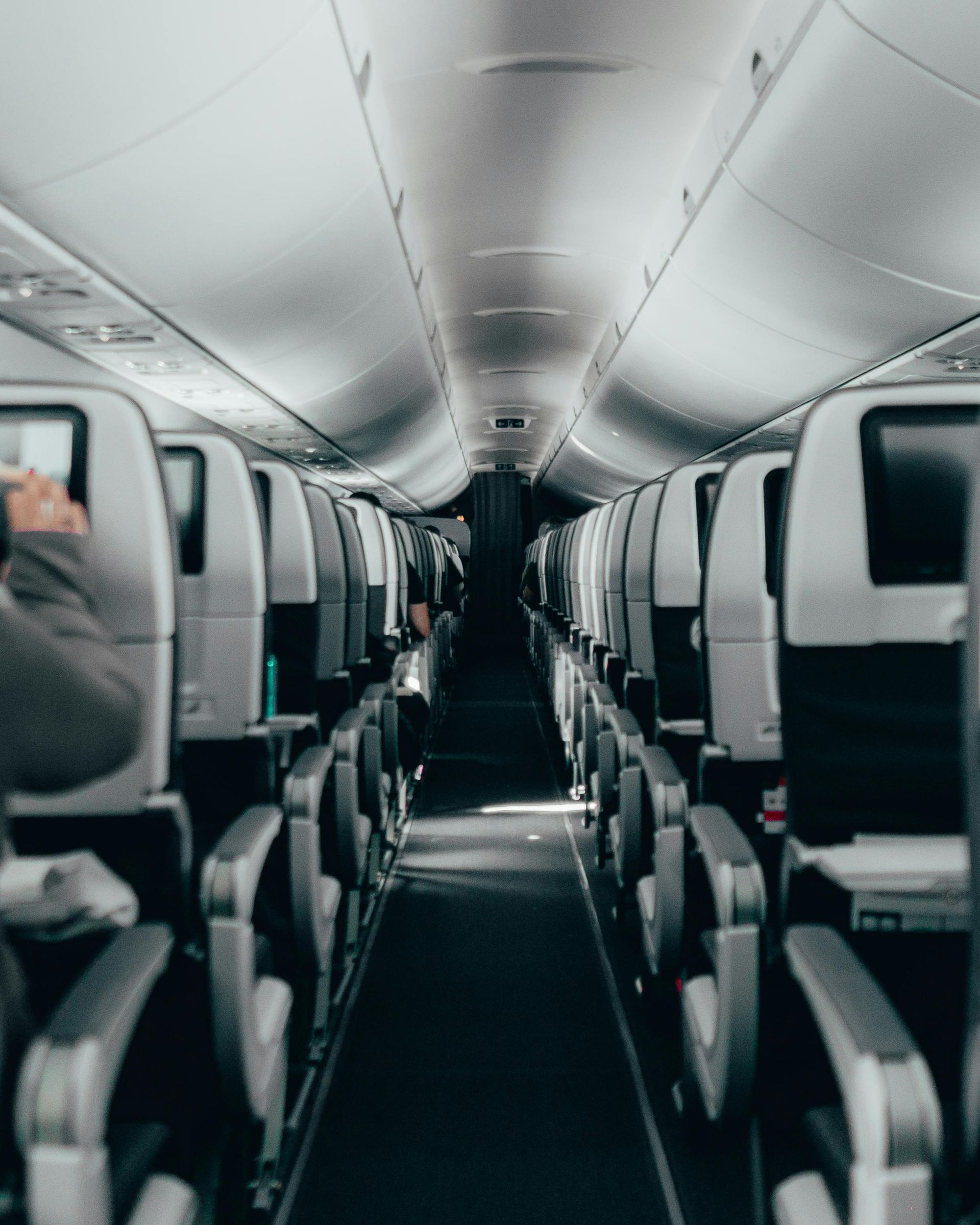 Interior view of an airplane cabin with rows of gray seats and a center aisle.
