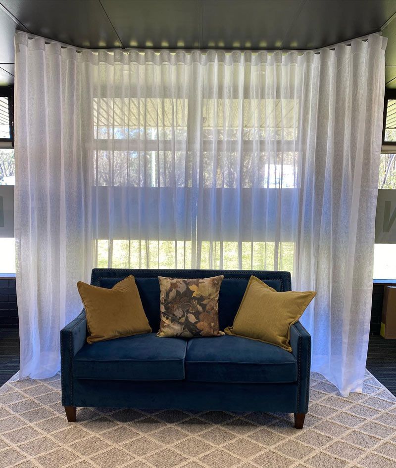 Spacious Window Adorned with White Curtains and a Blue Sofa with Pillows — Southern Blinds & Awnings In Balaclava NSW