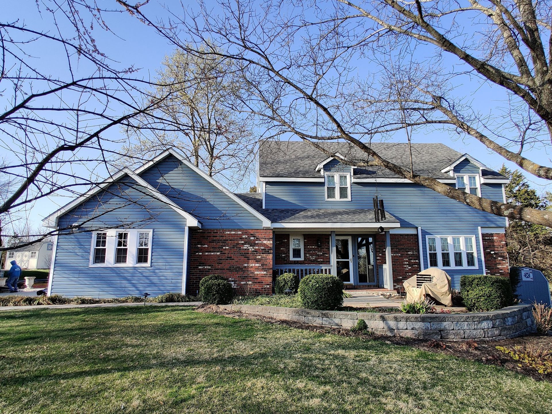 A blue house with a brick roof is sitting on top of a lush green field.