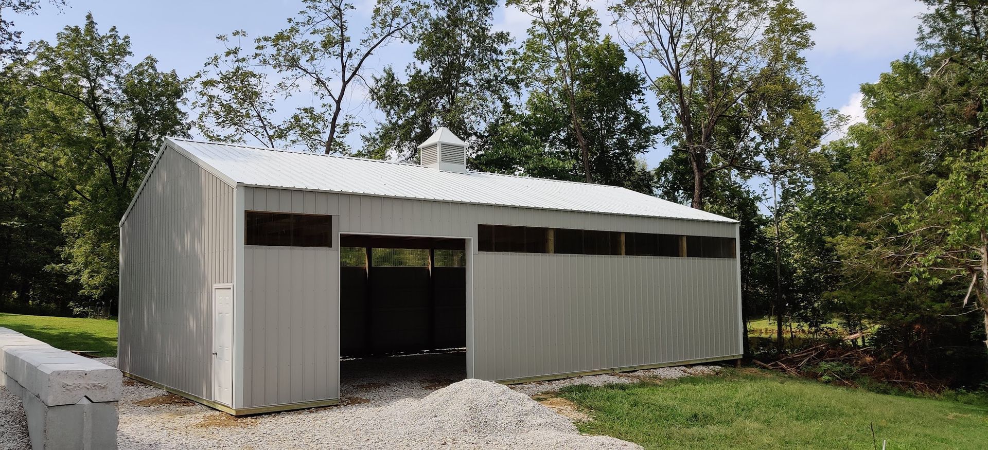 A large white barn is sitting in the middle of a grassy field.