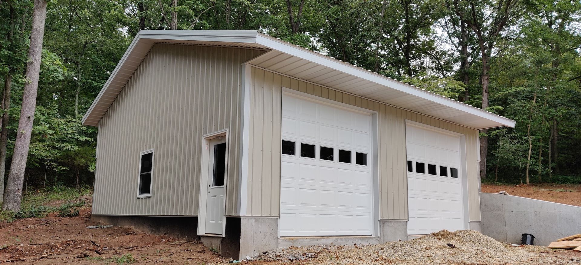 A garage with two white garage doors is sitting on top of a dirt hill.