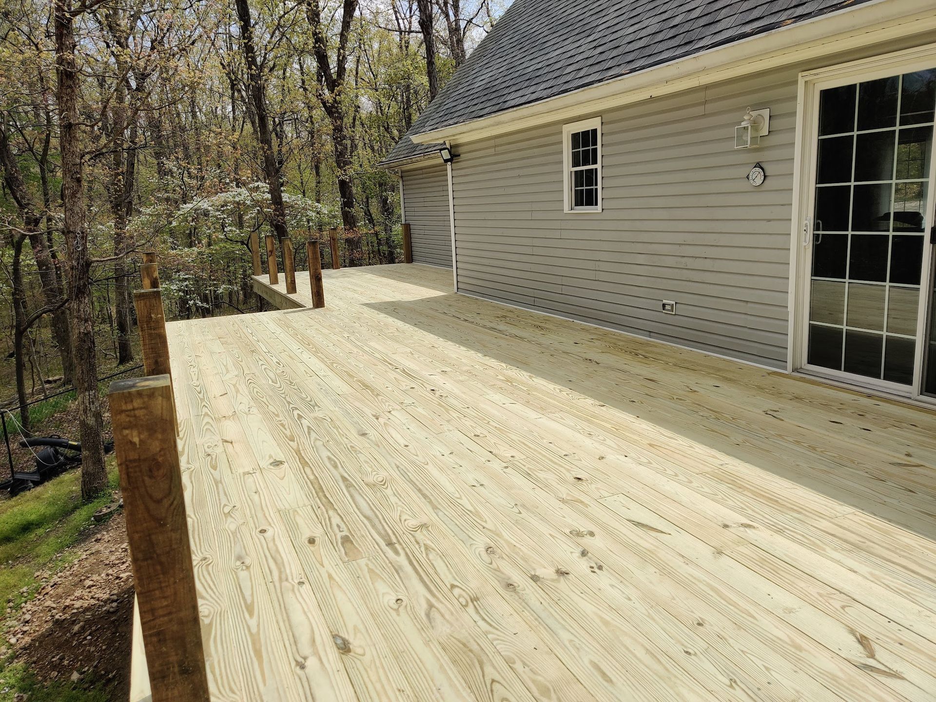 A large wooden deck is in front of a house surrounded by trees.