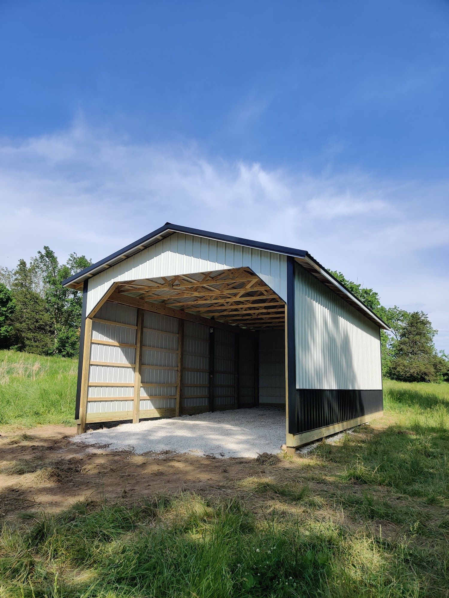 A white and black barn is sitting in the middle of a grassy field.