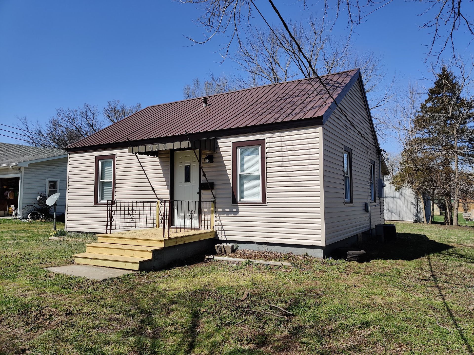 A small house with a brown roof is sitting in the middle of a grassy field.