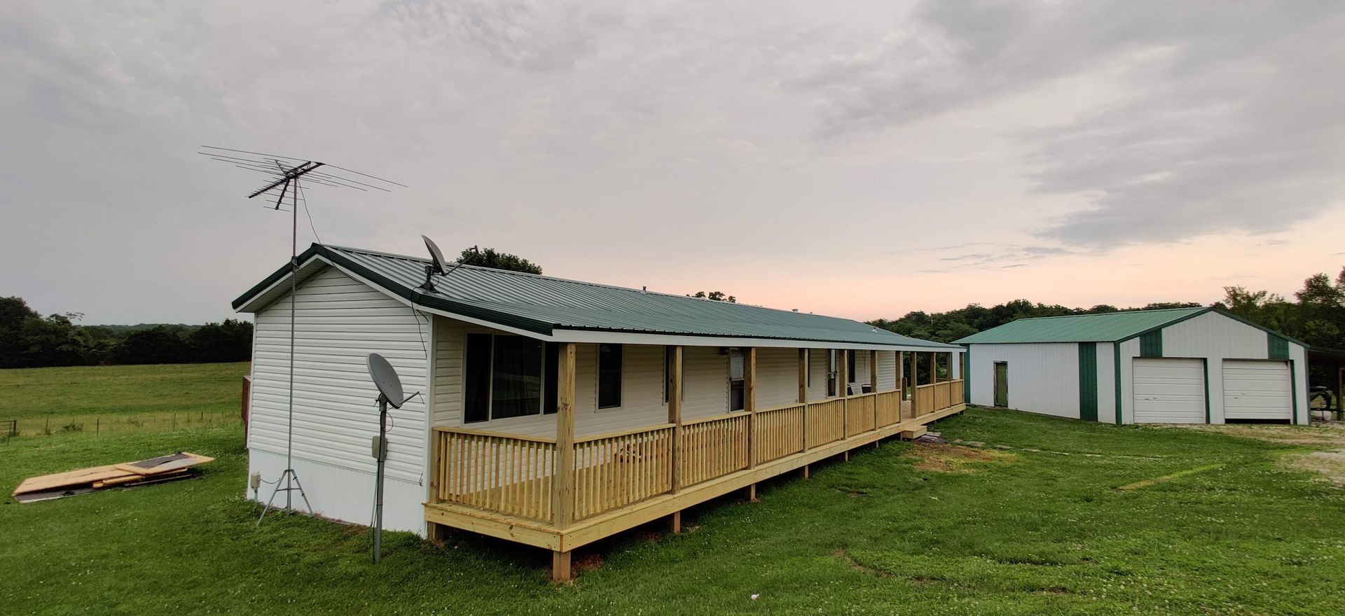 A mobile home with a green roof and a porch is sitting in the middle of a grassy field.