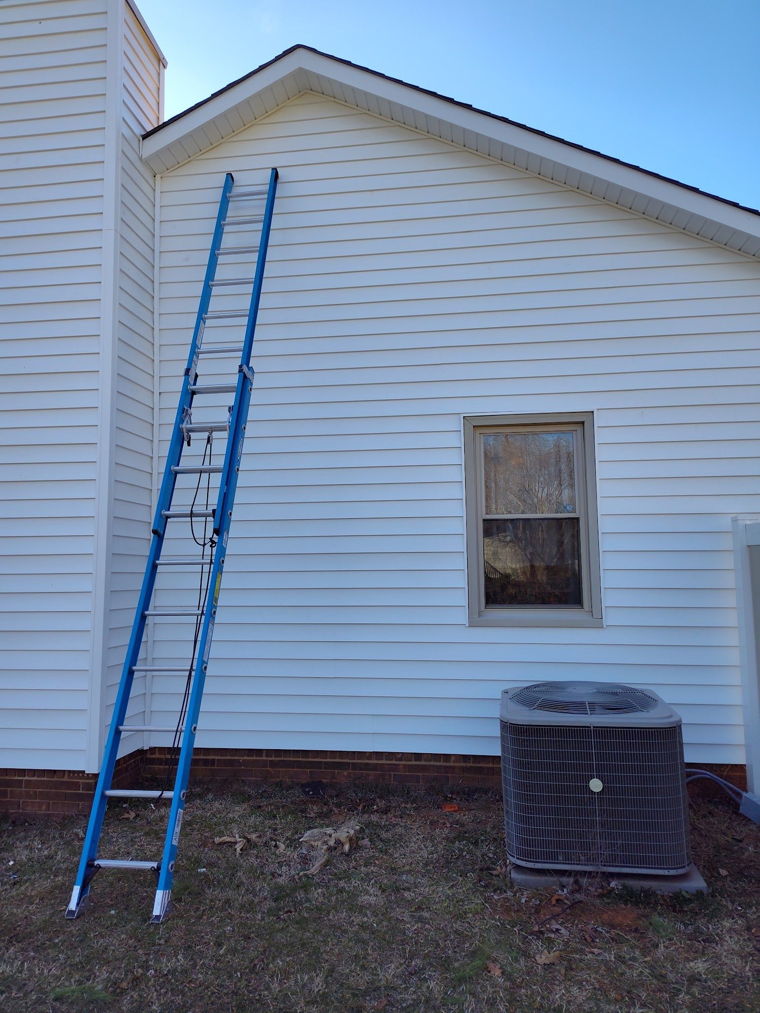 A blue ladder is leaning against the side of a white house.