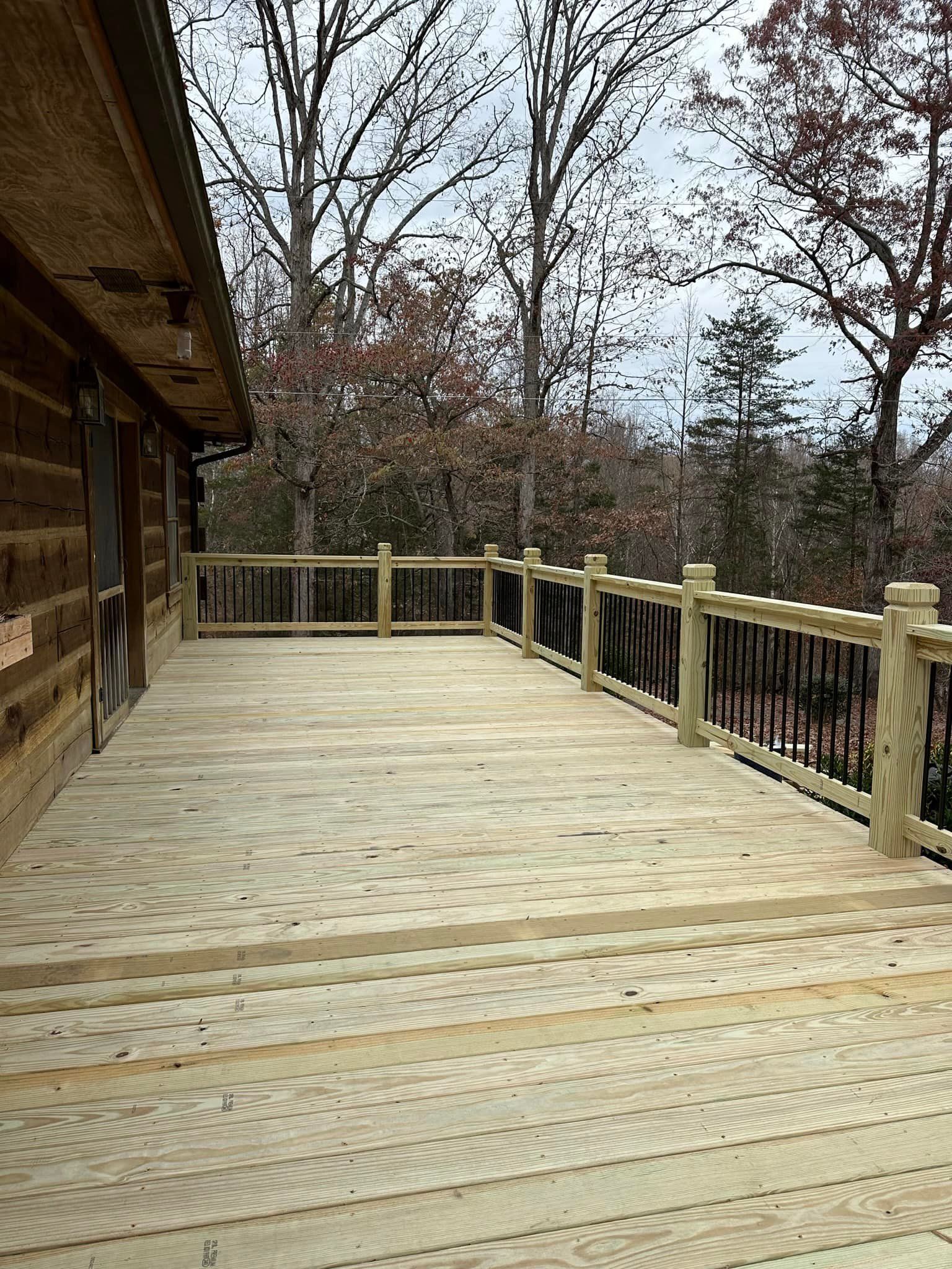 A large wooden deck with a railing and trees in the background.