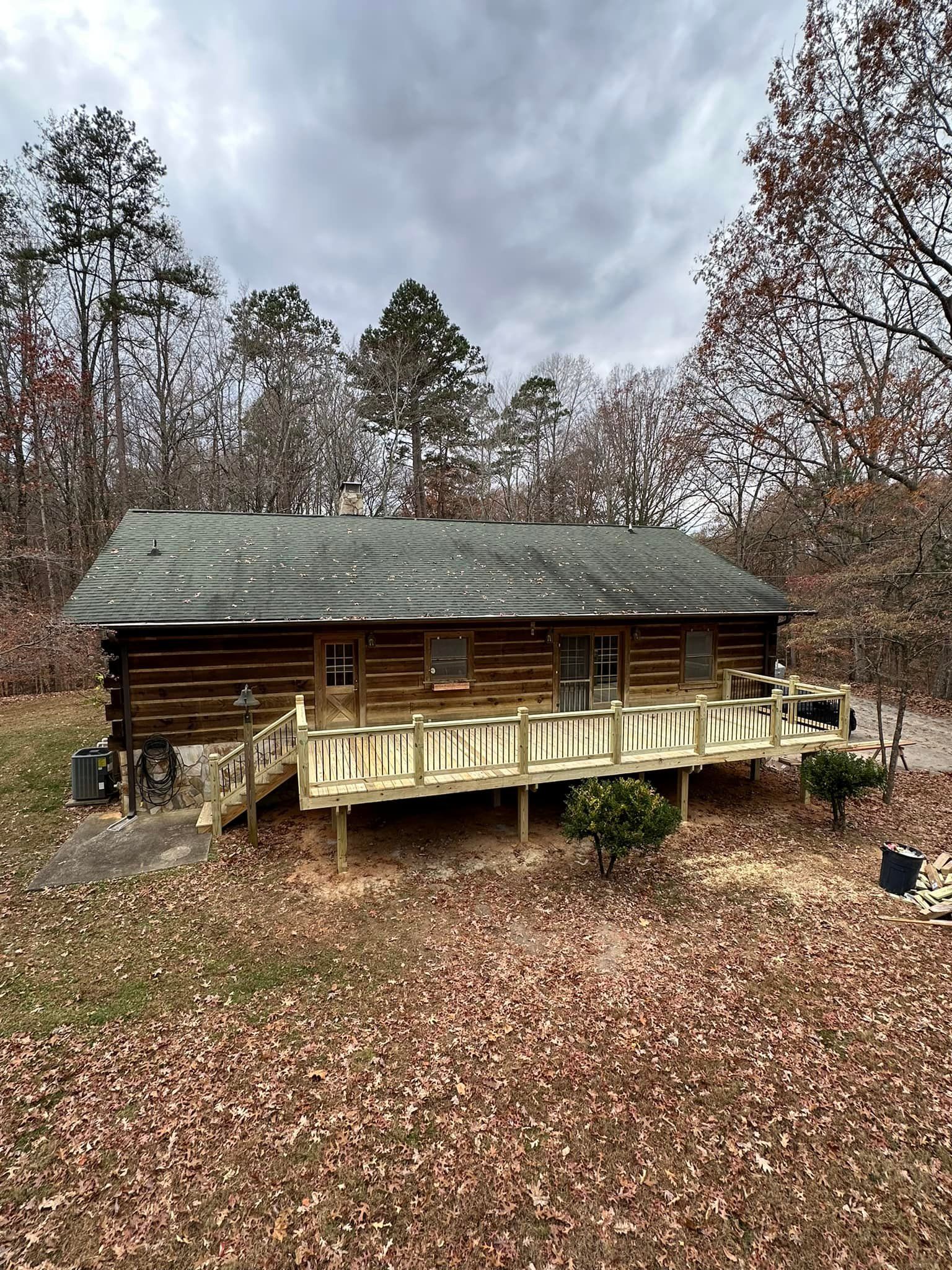 A log cabin with a large deck in the middle of the woods.