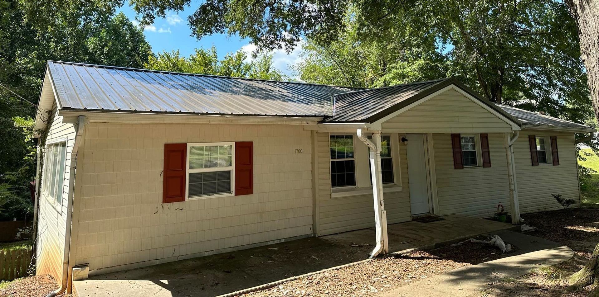 A small white house with red shutters and a metal roof.