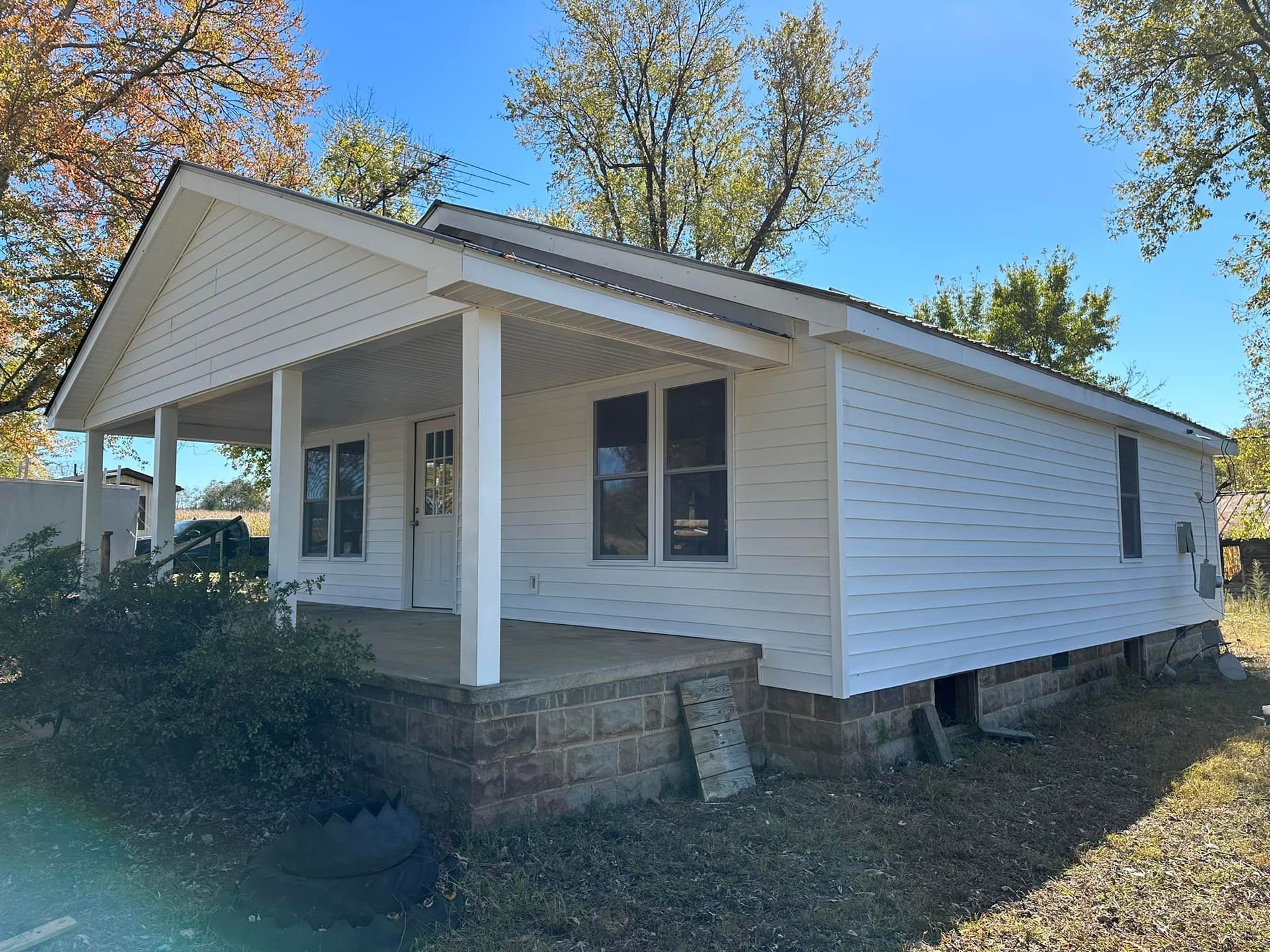 A small white house with a porch and trees in the background.