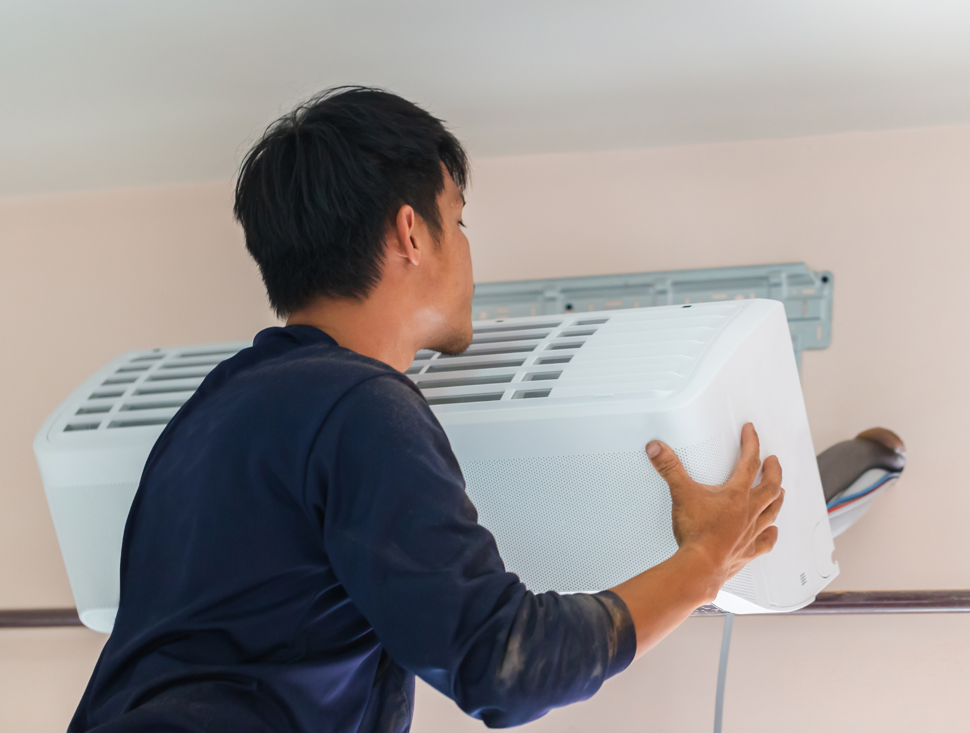 Man in blue shirt installing a white air conditioner unit on a wall.