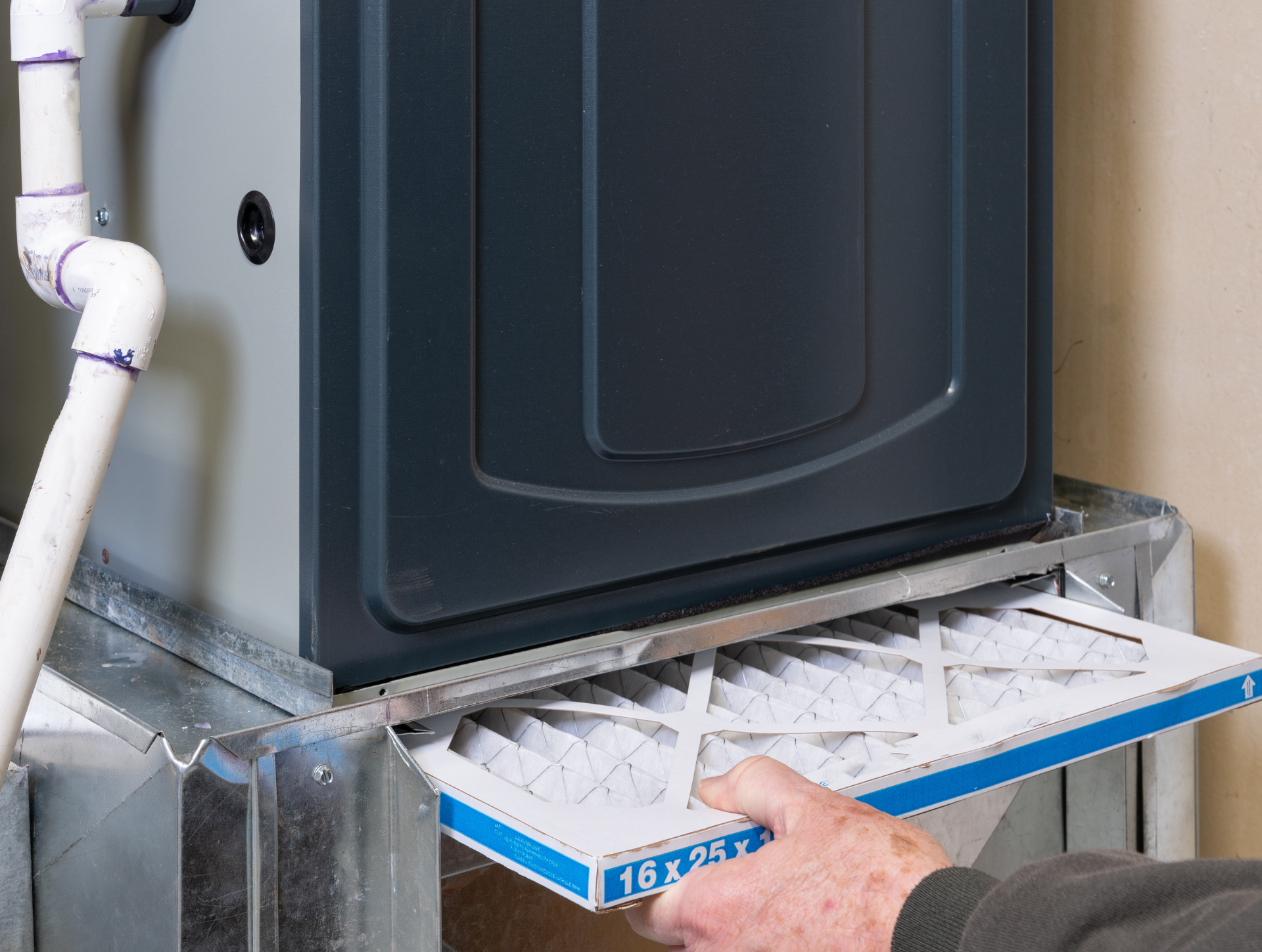 Person changes furnace air filter. Blue and white filter being pulled from metal housing.