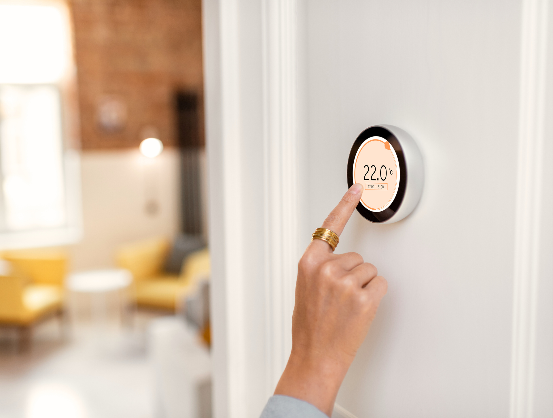 Person adjusting smart thermostat on a white wall in a home.