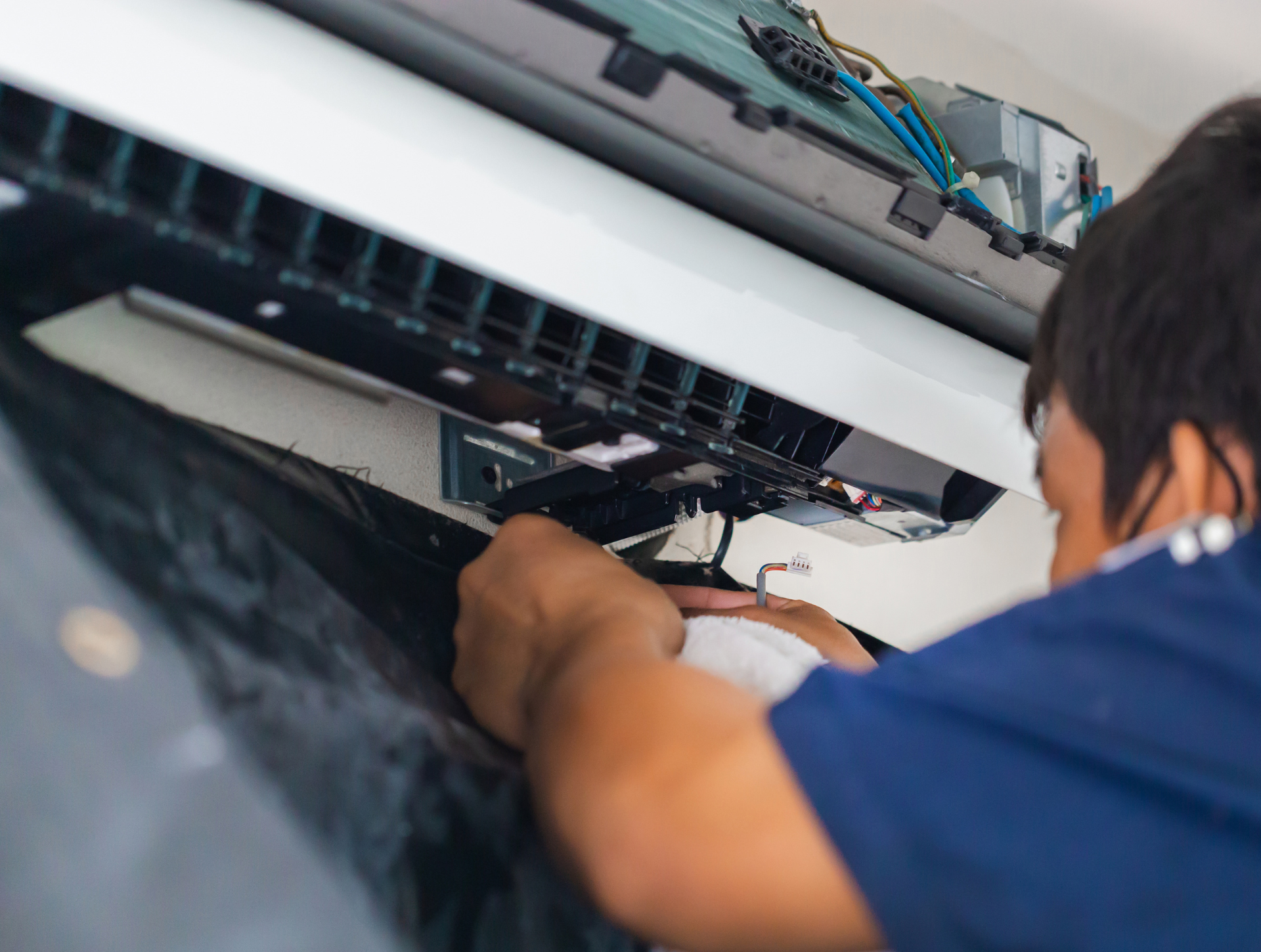 Man repairing an air conditioning unit; inside, with visible wires and tools.
