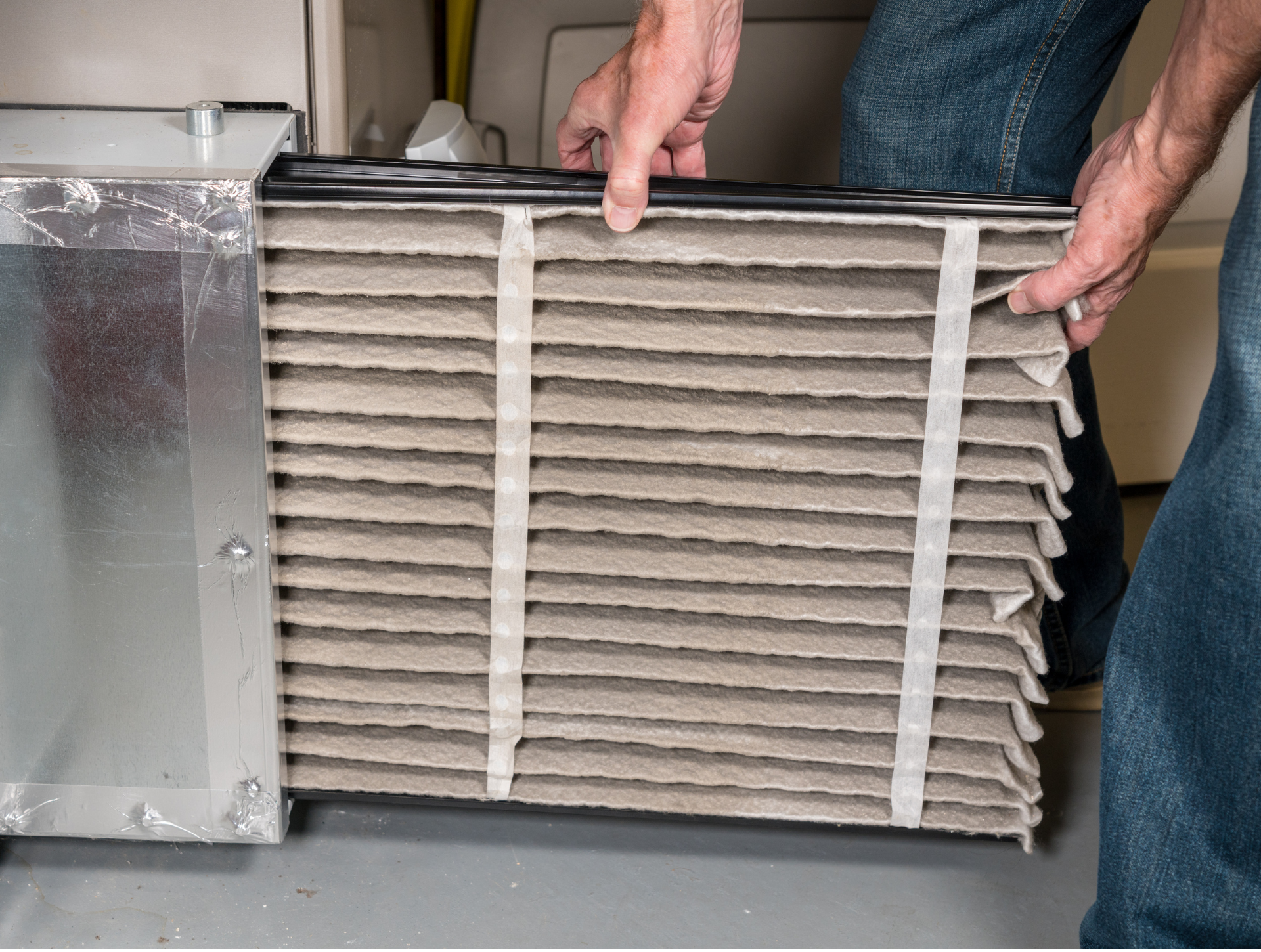 Person removing a dirty air filter from a furnace; hands holding the filter