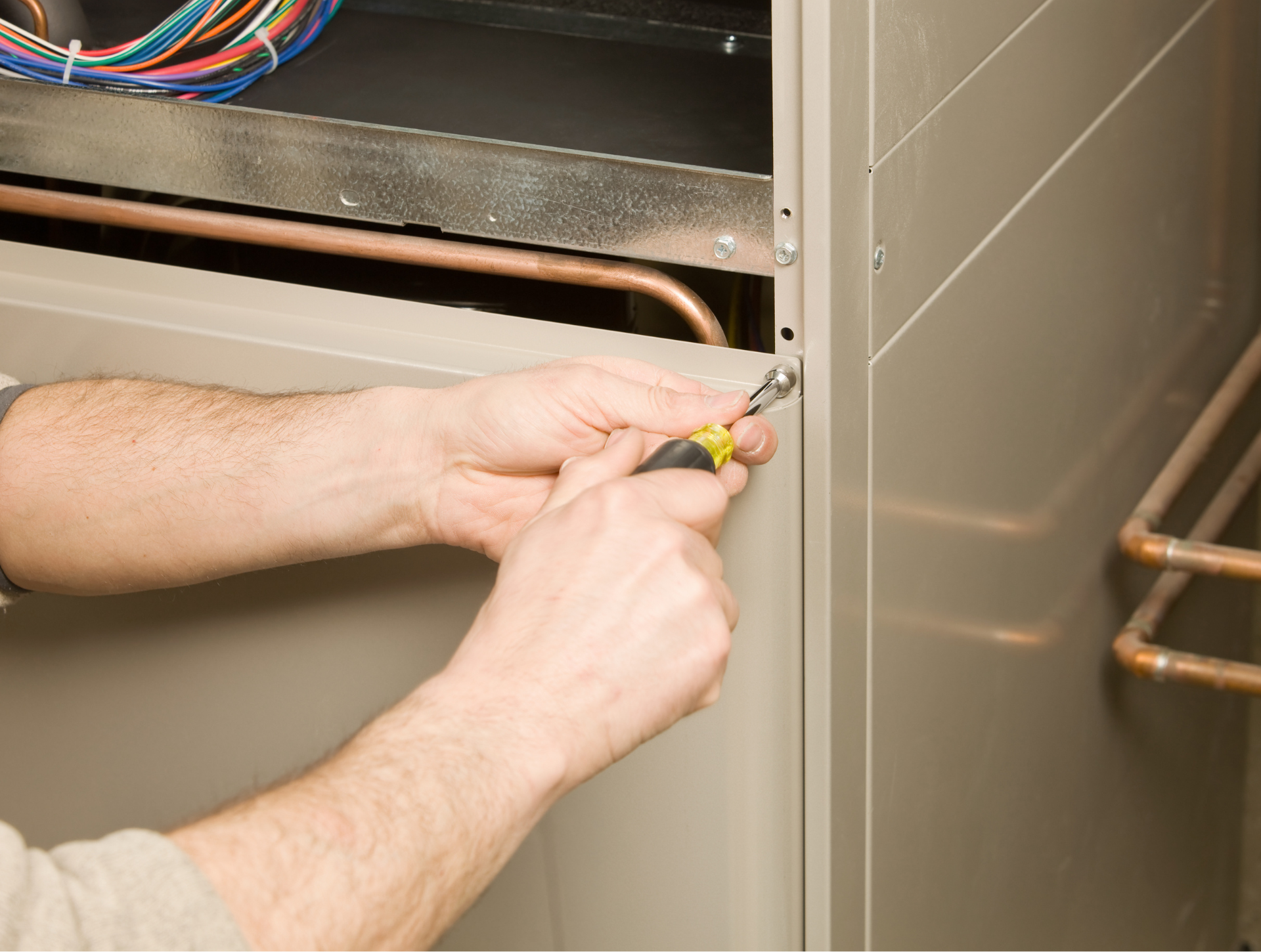 Person using a screwdriver on a metal panel, likely working on a furnace or HVAC system.