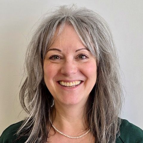 Woman with gray hair smiling, wearing a green top and pearl necklace.