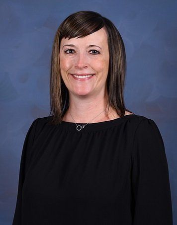 Woman with shoulder-length brown hair, smiling, wearing a black top, against a blue background.