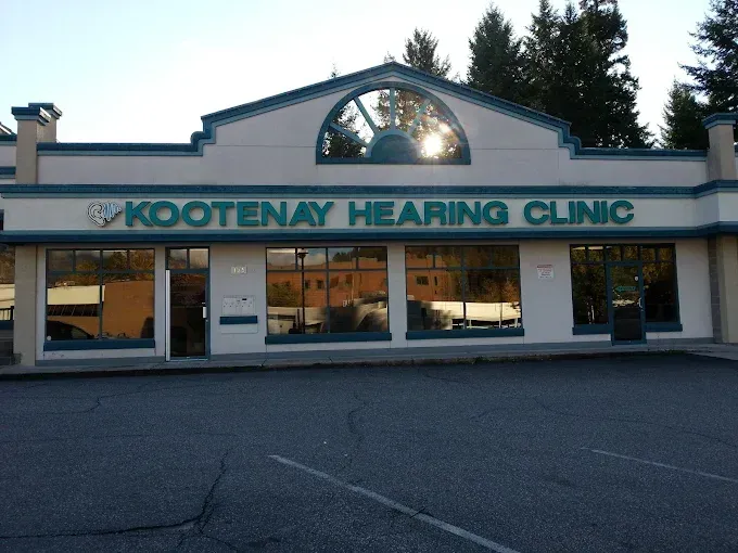 Kootenay Hearing Clinic building with green trim and sign, large windows, and parking lot.