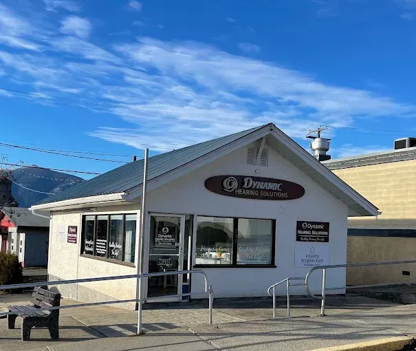 Exterior view of Dynamic Body & Spa business. White building with blue sky. Bench on sidewalk.
