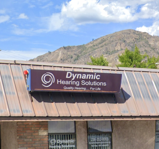 Sign for Dynamic Hearing Solutions on a building with a mountain backdrop.